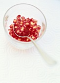 Pomegranate seeds in a small glass with a spoon