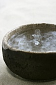 Drop of water falling into a stoneware bowl of water