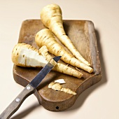Three parsnips on a wooden board with a knife