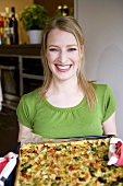 Young woman holding vegetable pizza on baking tray