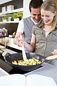 Man and woman stirring vegetables in wok