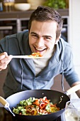 Young man tasting vegetables cooked in wok