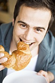 Young man biting into a croissant