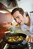 Young man tasting vegetables cooked in wok