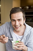 Young man eating yoghurt out of pot