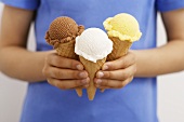 Hands holding three ice cream cones: chocolate, coconut, vanilla