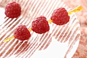 Raspberries on cocktail stick on glass plate