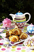 Hot cross buns & coloured Easter eggs on table laid for coffee