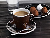 A cup of espresso with water and chocolate truffles
