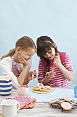 Two girls decorating biscuit lollies with icing sugar