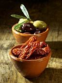 Dried tomatoes and olives in bowls on a wooden surface