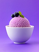 A scoop of blueberry ice cream with blueberries in white bowl