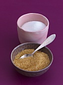 A bowl of white granulated sugar and a bowl of cane sugar