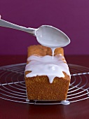 Icing being spooned over a loaf cake on a cake rack
