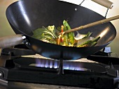 Vegetables being sautéed in a wok over a gas flame