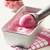 Raspberry ice cream in ice cream container with ice cream scoop