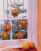 Mit Nelken gespickte Orangen hängen vor einem Fenster