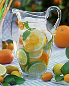 Jug of water with citrus fruit, lemon balm and ice cubes