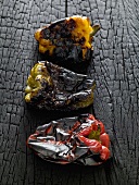 Three charred peppers on black wooden background