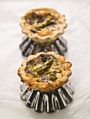 Two individual asparagus quiches on quiche tins