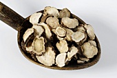Slices of red peony root on a wooden spoon