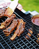 Brushing spare ribs on a grill with barbecue sauce