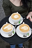 Woman carrying three cups of cappuccino on a tray