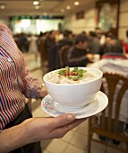 Woman serving a bowl of congee (rice porridge, China)