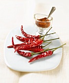 Dried chillies on white plate, chilli powder in glass