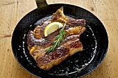 Fried prime rib of pork in a frying pan with rosemary