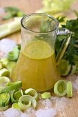 Vegetable stock in a glass jug with leeks, parsley and ice