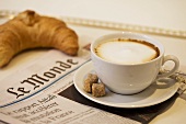 Milchkaffe auf französischer Zeitung mit einem Croissant