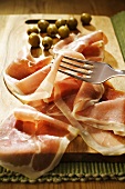 Prosciutto with green olives on a wooden board