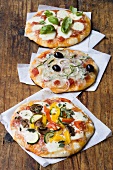 Three different pizzas on paper on wooden background