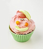 Cupcake with buttercream and amusing face made from sweets