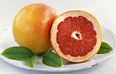 Whole grapefruit and half a grapefruit with leaves on a plate