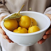 Hands holding a bowl of pickled lemons