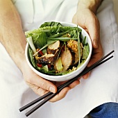 Man holding bowl of pork, salad leaves and peanuts