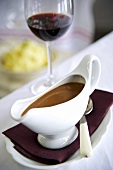 Gravy in a gravy boat with a glass of red wine in the background