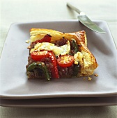 A piece of onion tart with vegetables and goat's cheese