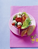 Tomaten-Mozzarella-Spieße auf grünem Salat, Schinken, Melone