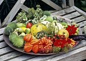 A dish of autumn fruits and flowers on a bench