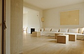 Schlichtes Wohnzimmer in Naturfarben gehalten mit langem Sofa und Sitzhocker auf Parkettboden