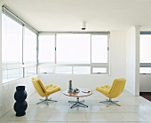 Zwei gelbe Sessel und ein runder Tisch im offenen Raum mit Eckfenster und Meeresblick