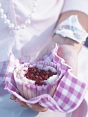 A woman holding a raspberry muffin in a napkin