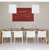 Ein großer Esstisch mit weißen Stühlen und zwei weiße Hängelampen vor rotes Bild an der Wand