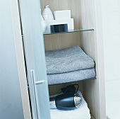 Towels and hair drier on shelves in a cupboard