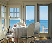 Raumecke mit Fenstern und Fenstertüren, mit einem runden Esstisch, Korbstühle und einen weiten Blick aufs Meer