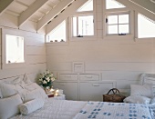 Großes Doppelbett in weiss gestrichenem Holzhäuschen mit Giebeldach