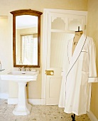 White dressing gown on tailor's dummy in nostalgic bathroom with pedestal sink and large, wood-framed mirror